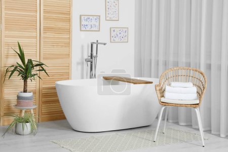 Téléchargez les photos : Élégante baignoire blanche et chaise avec serviettes dans la salle de bain. Design d'intérieur - en image libre de droit