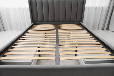 Cama moderna con espacio de almacenamiento para ropa de cama bajo base de listones en la habitación, primer plano