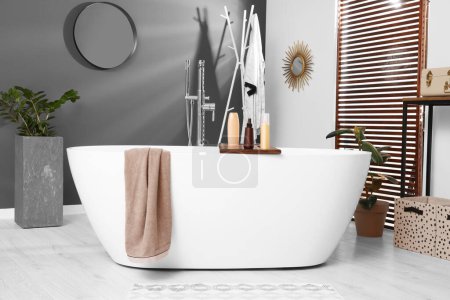 Foto de Elegante baño interior con bañera de cerámica, productos cosméticos y plantas de interior - Imagen libre de derechos