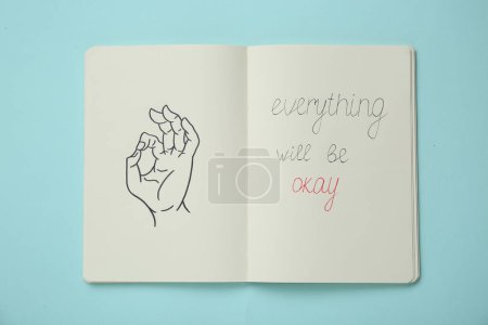 Foto de Cuaderno con frase Todo estará bien y dibujo de la mano mostrando gesto en turquesa claro, vista superior - Imagen libre de derechos