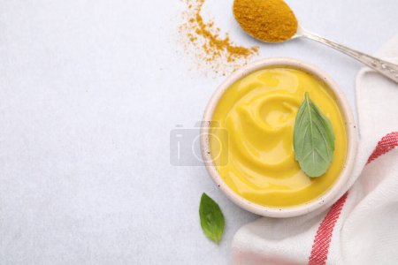 Tasty curry sauce, powder and basil leaves on light table, flat lay. Space for text
