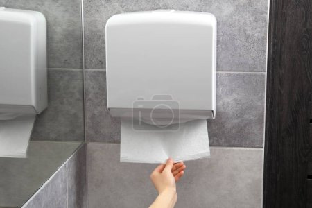 Mujer tomando nueva toalla de papel fresco del dispensador en el baño, primer plano