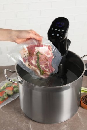 Photo for Woman putting vacuum packed meat into pot with sous vide cooker, closeup. Thermal immersion circulator - Royalty Free Image