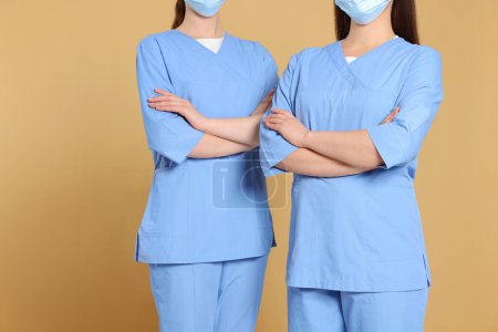 Photo for Nurses wearing medical uniforms on light brown background, closeup - Royalty Free Image
