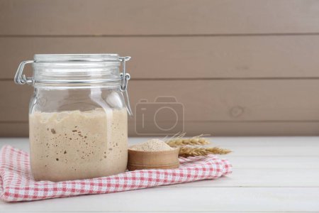 Leaven and ears of wheat on white wooden table, space for text