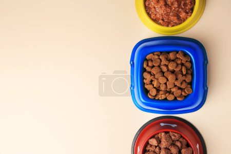Téléchargez les photos : Nourriture sèche et humide pour animaux de compagnie dans des bols d'alimentation sur fond beige, plat. Espace pour le texte - en image libre de droit