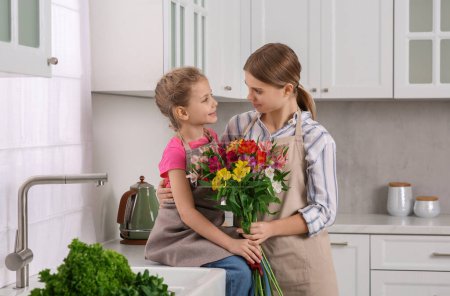 Photo for Little daughter congratulating mom with bouquet of flowers in kitchen. Happy Mother's Day - Royalty Free Image