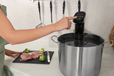 Foto de Mujer utilizando circulador de inmersión térmica en la cocina, primer plano. Sous vide cocinar - Imagen libre de derechos