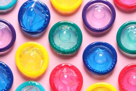 Colorful condoms on pink background, flat lay