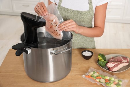 Femme mettant la viande emballée sous vide dans un pot avec cuisinière sous vide à l'intérieur, gros plan. Cirateur d'immersion thermique