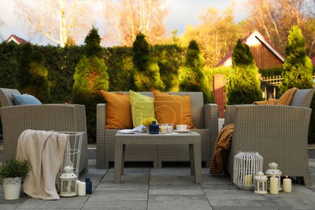 Schöne Gartenmöbel aus Rattan, weiche Kissen und verschiedene Dekorelemente im Hinterhof