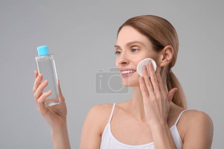 Foto de Hermosa mujer quitando maquillaje con almohadilla de algodón sobre fondo gris - Imagen libre de derechos