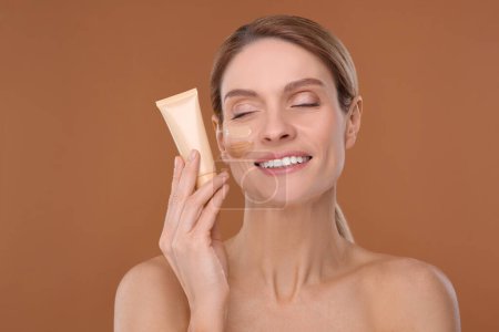 Photo for Woman holding tube of foundation on brown background - Royalty Free Image