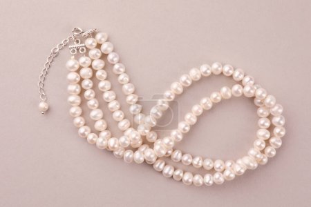 Elegant pearl necklace on beige background, top view