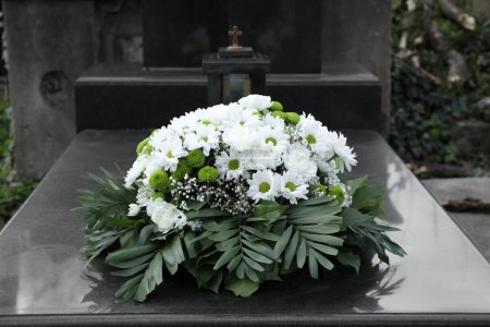 Téléchargez les photos : Couronne funéraire de fleurs sur pierre tombale de granit dans le cimetière - en image libre de droit
