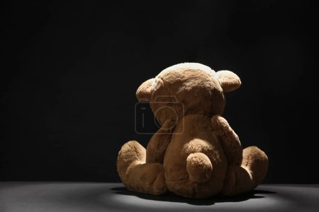 Niedlicher einsamer Teddybär auf dunklem Hintergrund, Rückansicht. Raum für Text