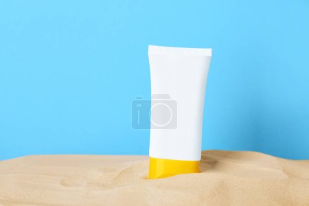 Téléchargez les photos : Produit bronzant dans le sable sur fond bleu clair. Espace pour le texte - en image libre de droit