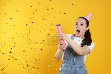 Photo for Young woman blowing up party popper on yellow background - Royalty Free Image