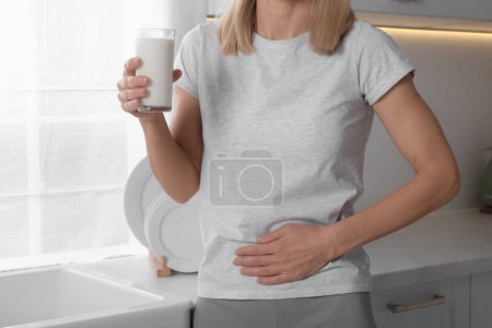Woman with glass of milk suffering from lactose intolerance in kitchen, closeup