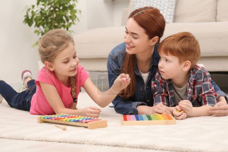 Mère heureuse et les enfants jouent avec différents kits de jeu de mathématiques sur le sol dans la chambre. Étudier les mathématiques avec plaisir