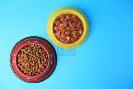 Photo for Wet and dry pet food in feeding bowls on light blue background, flat lay. Space for text - Royalty Free Image