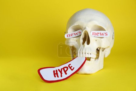 Téléchargez les photos : Crâne humain avec des cartes en papier avec des mots Hype et Nouvelles sur fond jaune - en image libre de droit
