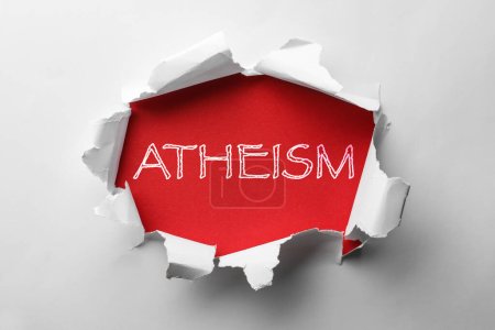 Téléchargez les photos : Mot Athéisme sur fond rouge, vue à travers le trou dans le papier blanc - en image libre de droit
