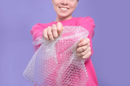 Photo for Woman popping bubble wrap on purple background, closeup. Stress relief - Royalty Free Image