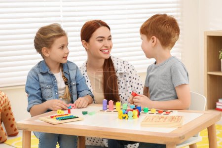 Happy mother and children playing with different math game kits at desk in room. Study mathematics with pleasure