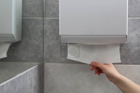 Téléchargez les photos : Femme prenant une nouvelle serviette de papier frais du distributeur dans la salle de bain, gros plan. Espace pour le texte - en image libre de droit