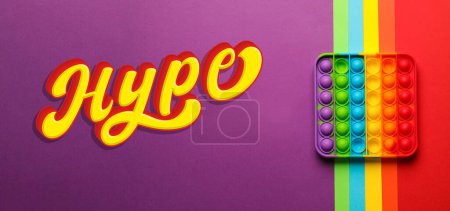 Téléchargez les photos : Mot Hype et arc-en-ciel pop il fidget jouet sur fond de couleur, vue de dessus. Conception de bannière - en image libre de droit