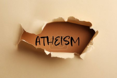 Palabra ateísmo sobre fondo marrón, vista a través del agujero en papel beige