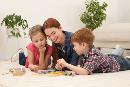 Mère heureuse et les enfants jouent avec différents kits de jeu de mathématiques sur le sol dans la chambre. Étudier les mathématiques avec plaisir