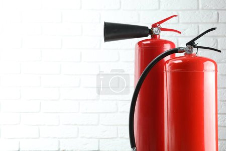 Fire extinguishers against white brick wall, closeup. Space for text
