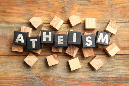Word Atheism made of black cubes with letters on wooden table, flat lay