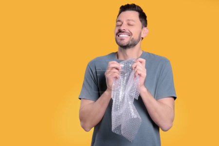 Man popping bubble wrap on yellow background, space for text. Stress relief