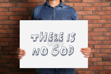 Téléchargez les photos : L'athéisme. Homme tenant signe avec le texte Il n'y a pas de Dieu près du mur de briques, gros plan - en image libre de droit