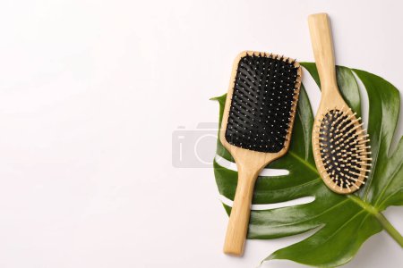 Wooden hairbrushes and green leaf on white background, flat lay. Space for text