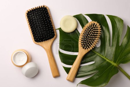 Téléchargez les photos : Brosses à cheveux en bois, produits cosmétiques et feuilles vertes sur fond blanc, pose plate - en image libre de droit