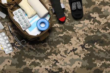 Flat lay composition with military first aid kit on camouflage fabric. Space for text