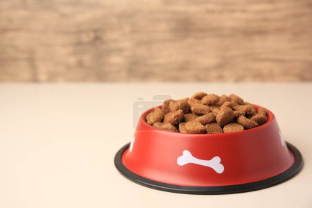 Dry dog food in feeding bowl on beige table. Space for text