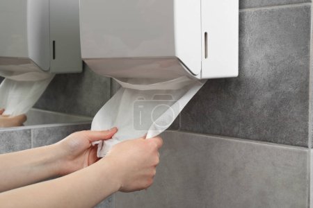 Woman taking new fresh paper towel from dispenser in bathroom, closeup