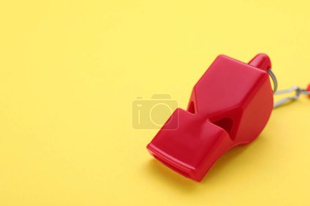 One red whistle on yellow background, closeup. Space for text