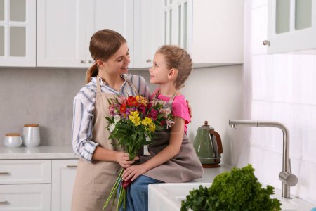 Foto de Hijita felicitando a mamá con ramo de flores en la cocina. Feliz Día de la Madre - Imagen libre de derechos