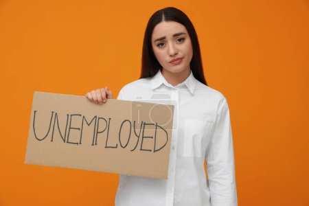 Foto de Young woman holding sign with word Unemployed on orange background - Imagen libre de derechos