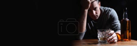 Suffering from hangover. Man with alcoholic drink at table against black background, selective focus. Banner design with space for text