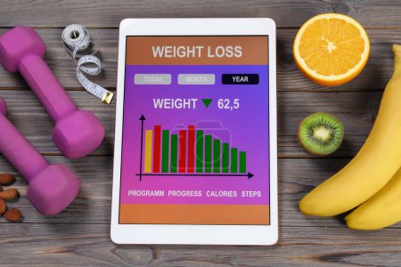 Photo for Tablet with weight loss calculator application, dumbbells and products on grey wooden table, above view - Royalty Free Image