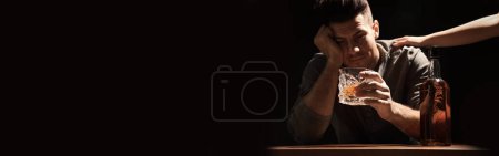 Suffering from hangover. Man with glass of alcoholic drink at table against black background, selective focus. Banner design with space for text