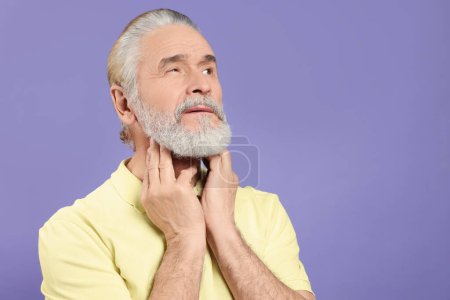 Téléchargez les photos : Homme âgé souffrant de maux de gorge sur fond violet clair, espace pour le texte. Symptômes de froid - en image libre de droit