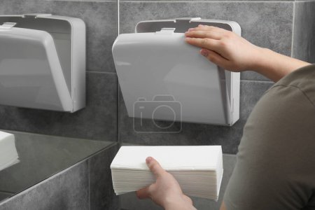 Woman putting new fresh paper towels into dispenser in bathroom, closeup